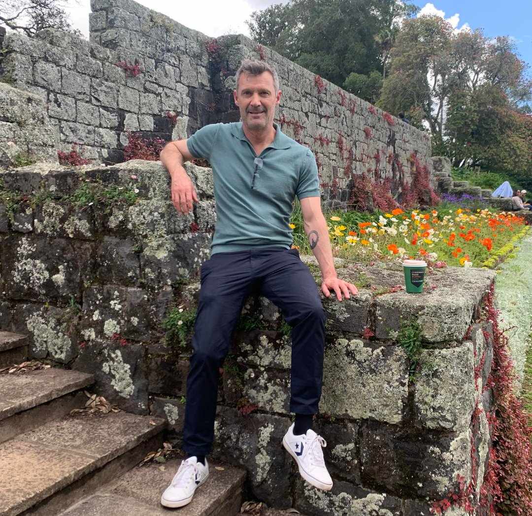 Photo of Andre, sitting on a stone wall with a coffee
